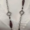 Collar largo plateado con detalles geométricos y cuentas burdeos