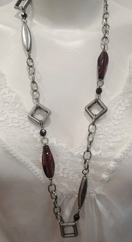 Collar largo plateado con detalles geométricos y cuentas burdeos